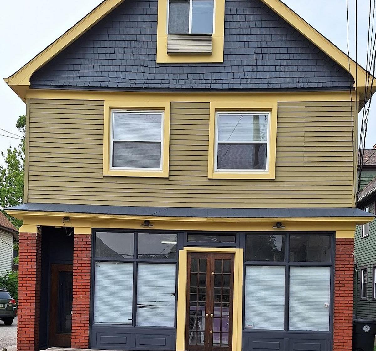 The same building finished, with a dark slate gable, olive siding, yellow trim picked out around the windows and the brick storefront below.