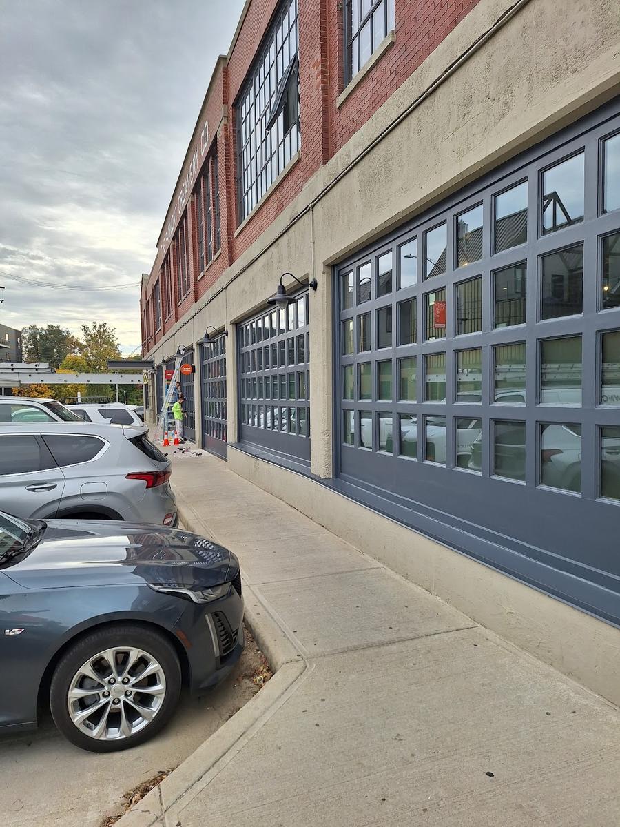 A row of gray-framed window bays along the side of a brick and stucco commercial building, with a crew member on a ladder in the distance.